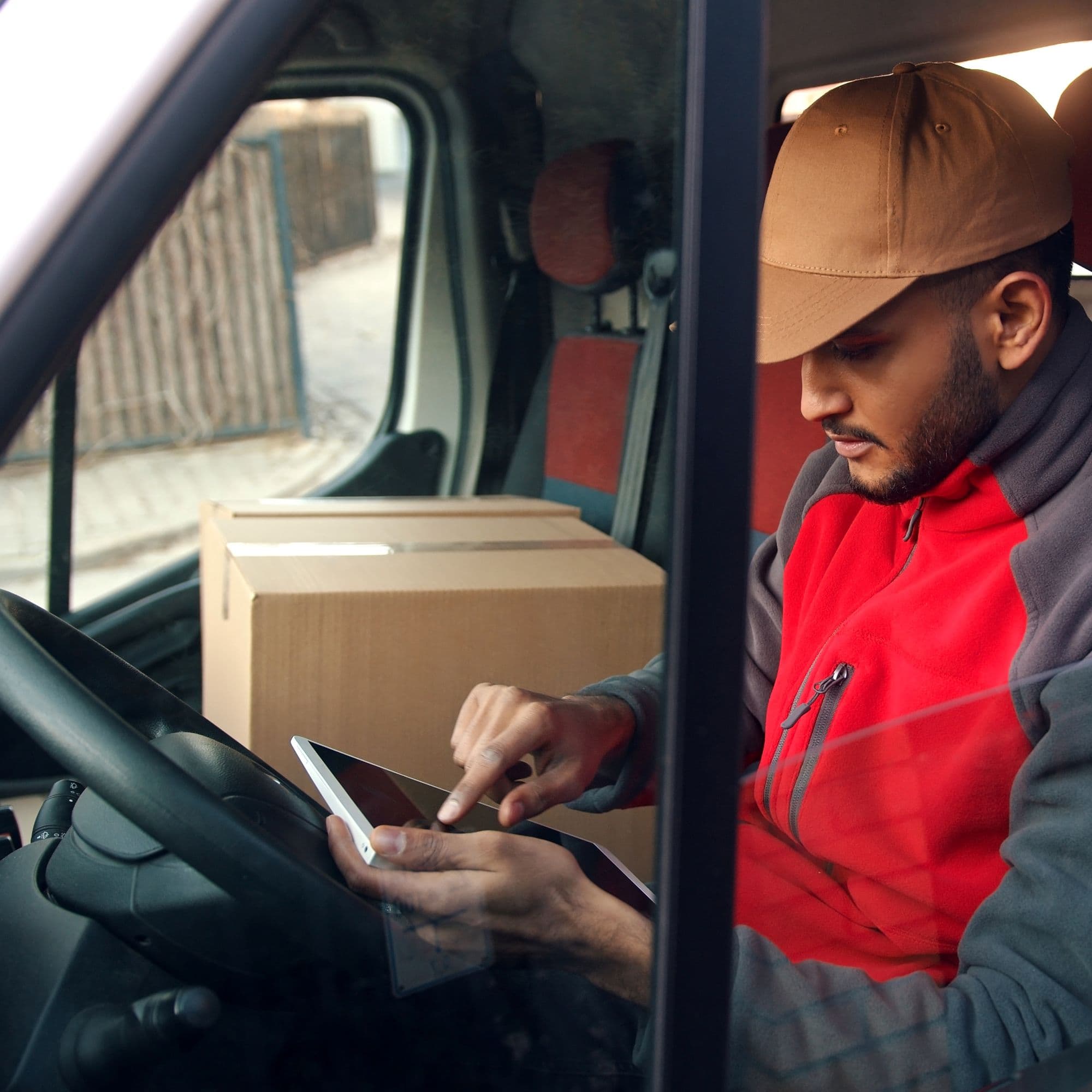A delivery driver using a smartphone inside a van with packages beside him. A delivery driver using a smartphone inside a van with packages beside him.