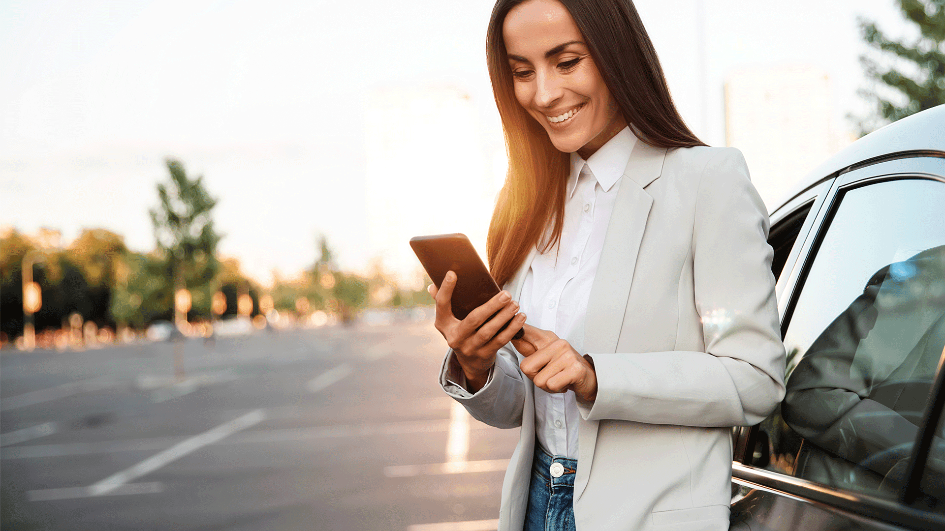 A professional woman using a smartphone while standing beside a car. A professional woman using a smartphone while standing beside a car.