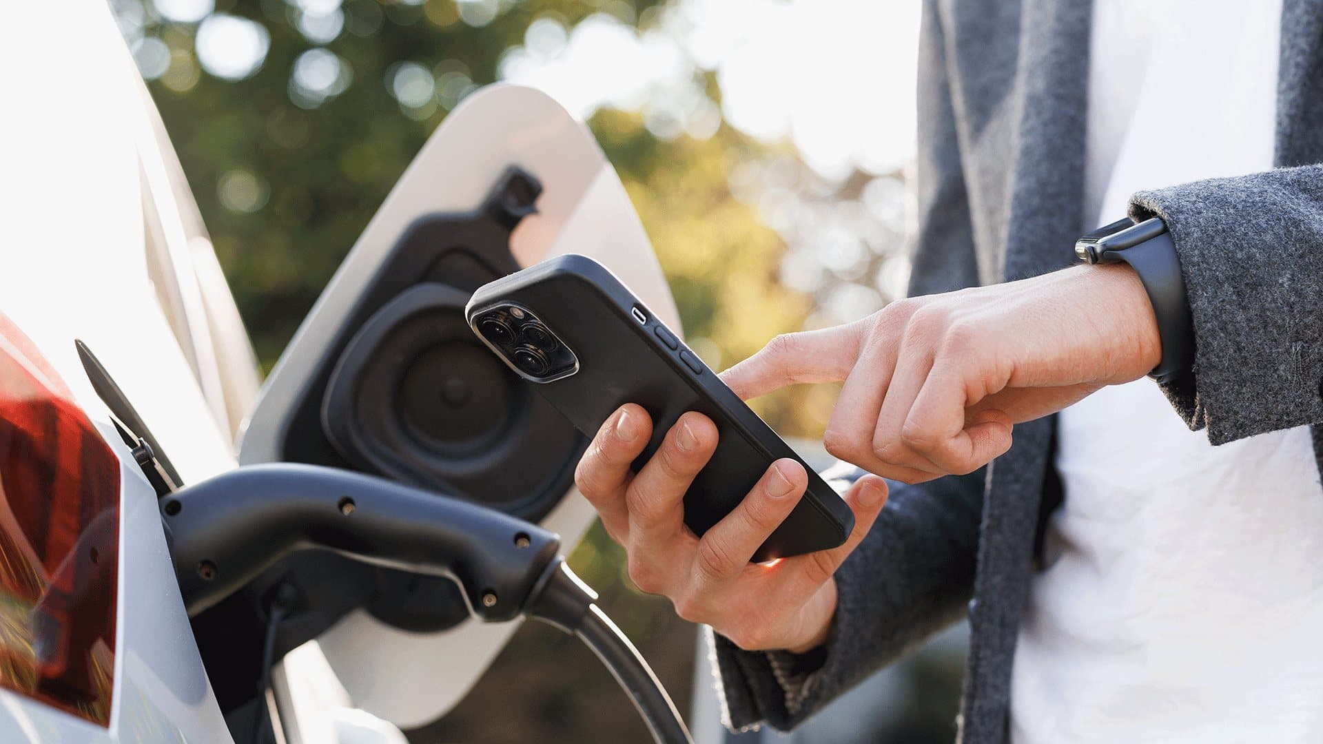 A person using a smartphone while charging an electric vehicle. A person using a smartphone while charging an electric vehicle.