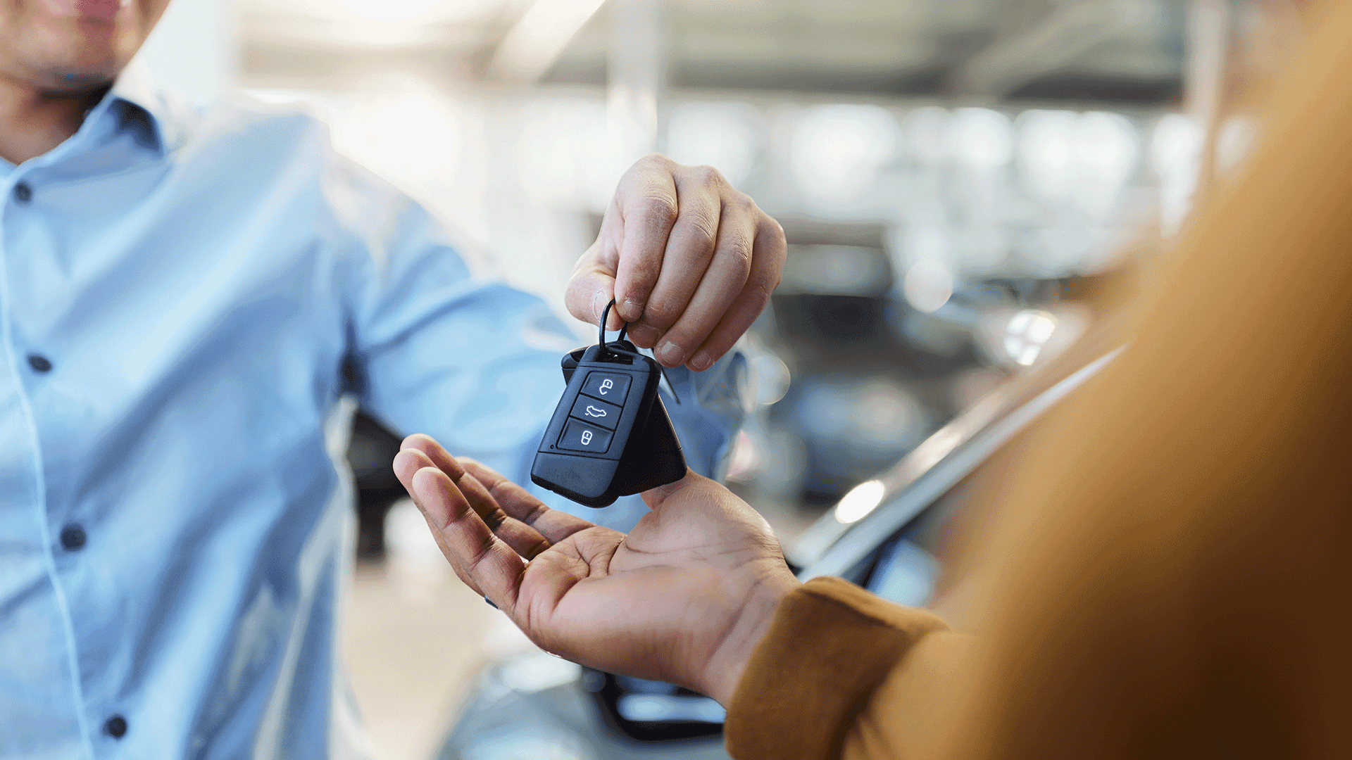 A person handing car keys to a customer at a vehicle dealership. A person handing car keys to a customer at a vehicle dealership.