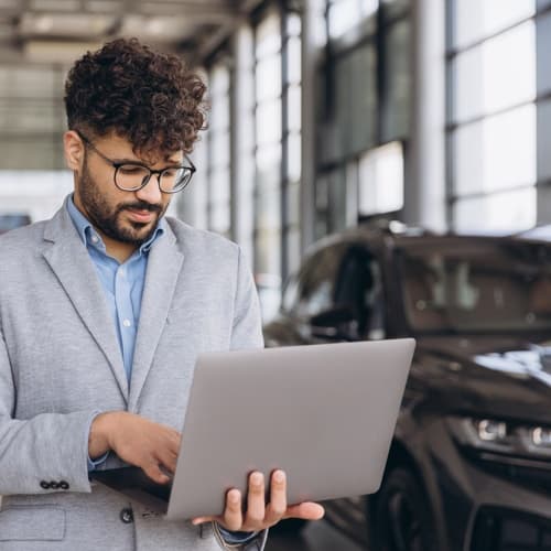 car salesman working on laptop in car dealership car salesman working on laptop in car dealership