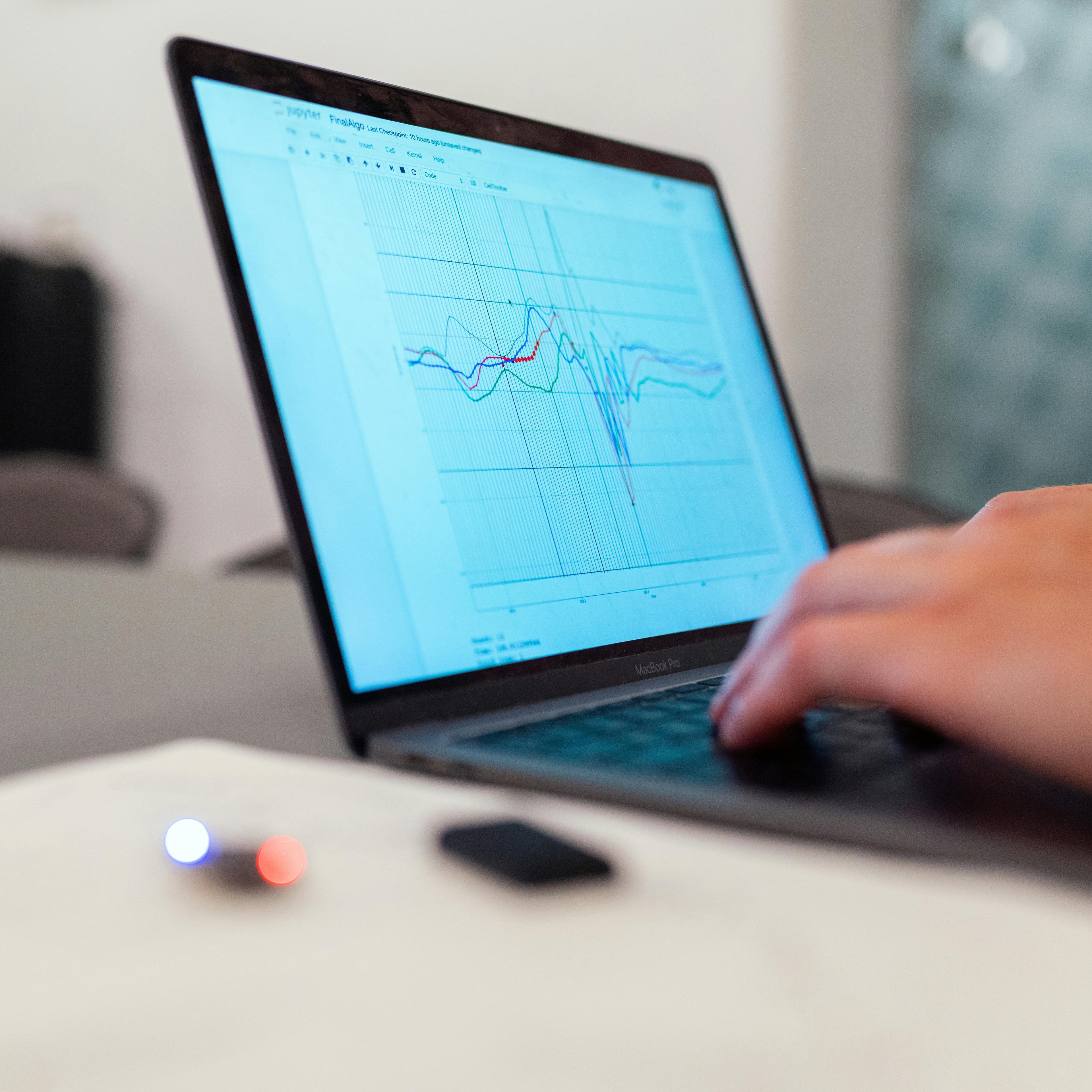 A person using a laptop displaying a graph with multiple colored data lines on the screen. A person using a laptop displaying a graph with multiple colored data lines on the screen.