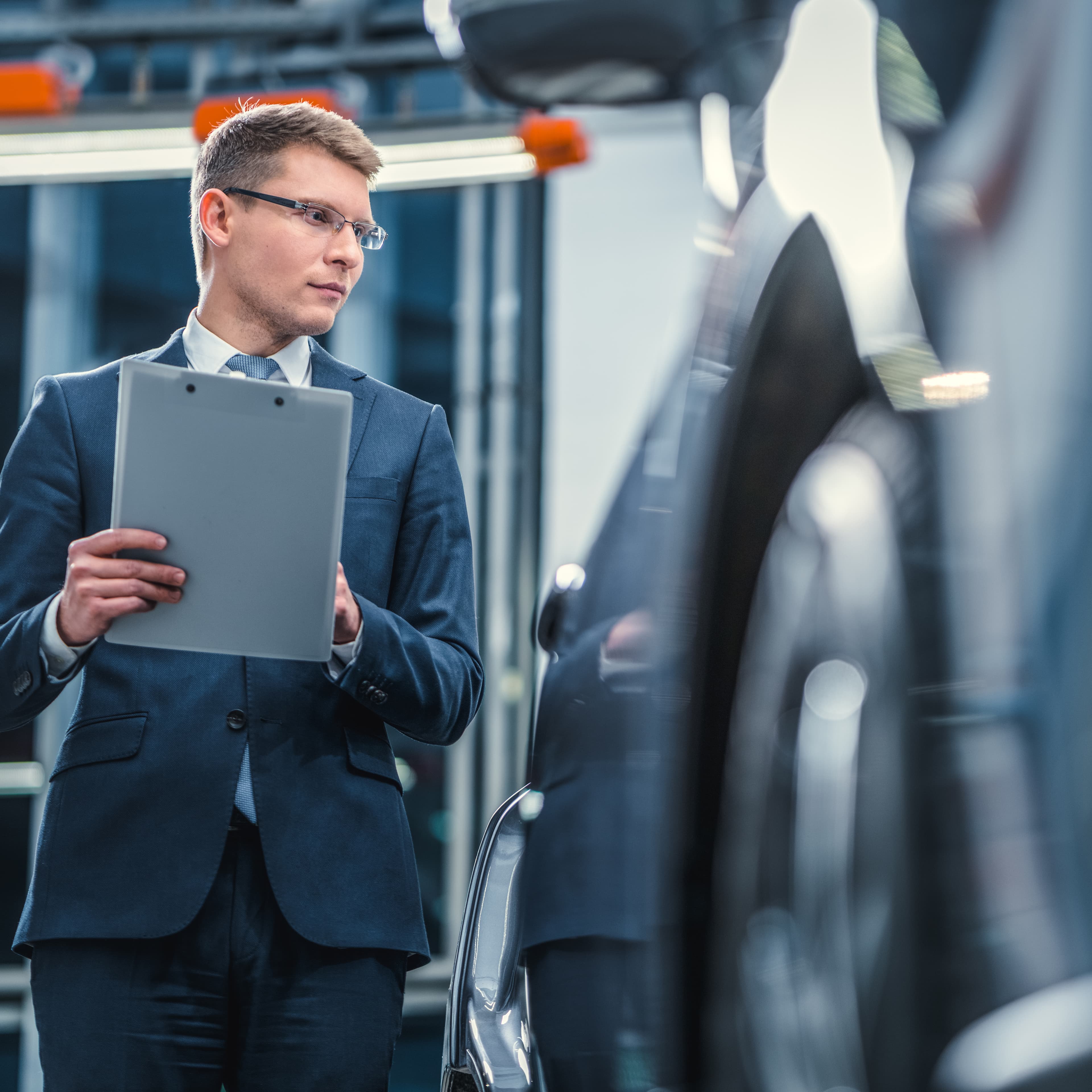 A professional holding a tablet while inspecting vehicles at an automotive facility. A professional holding a tablet while inspecting vehicles at an automotive facility.