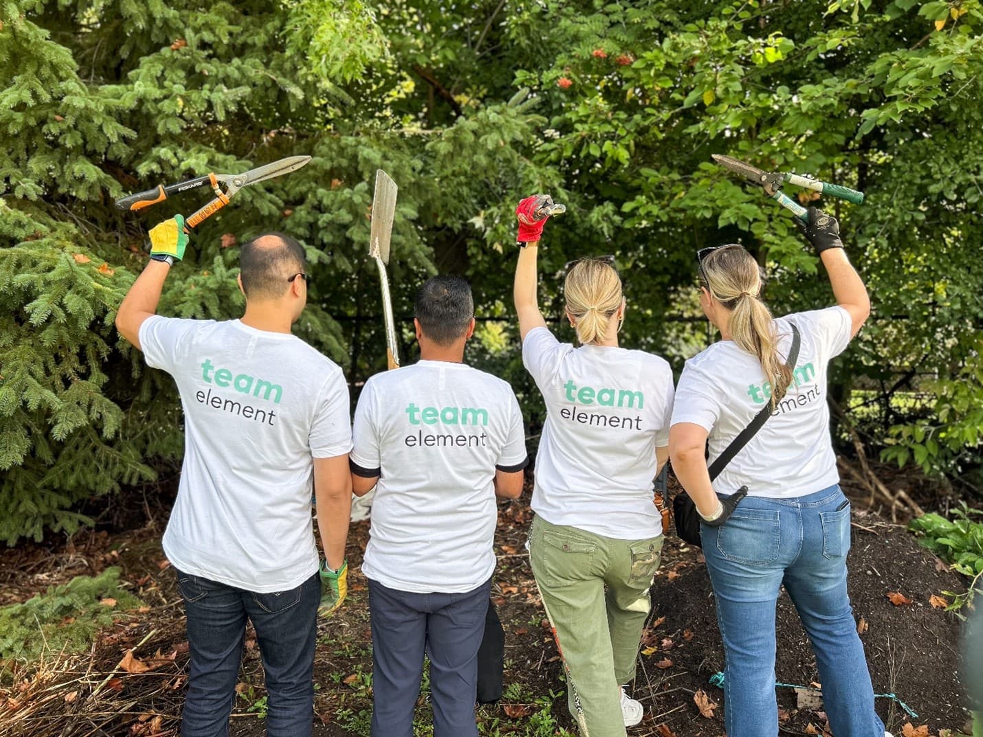Employees participating in a community beautification project, holding gardening tools outdoors. Employees participating in a community beautification project, holding gardening tools outdoors.