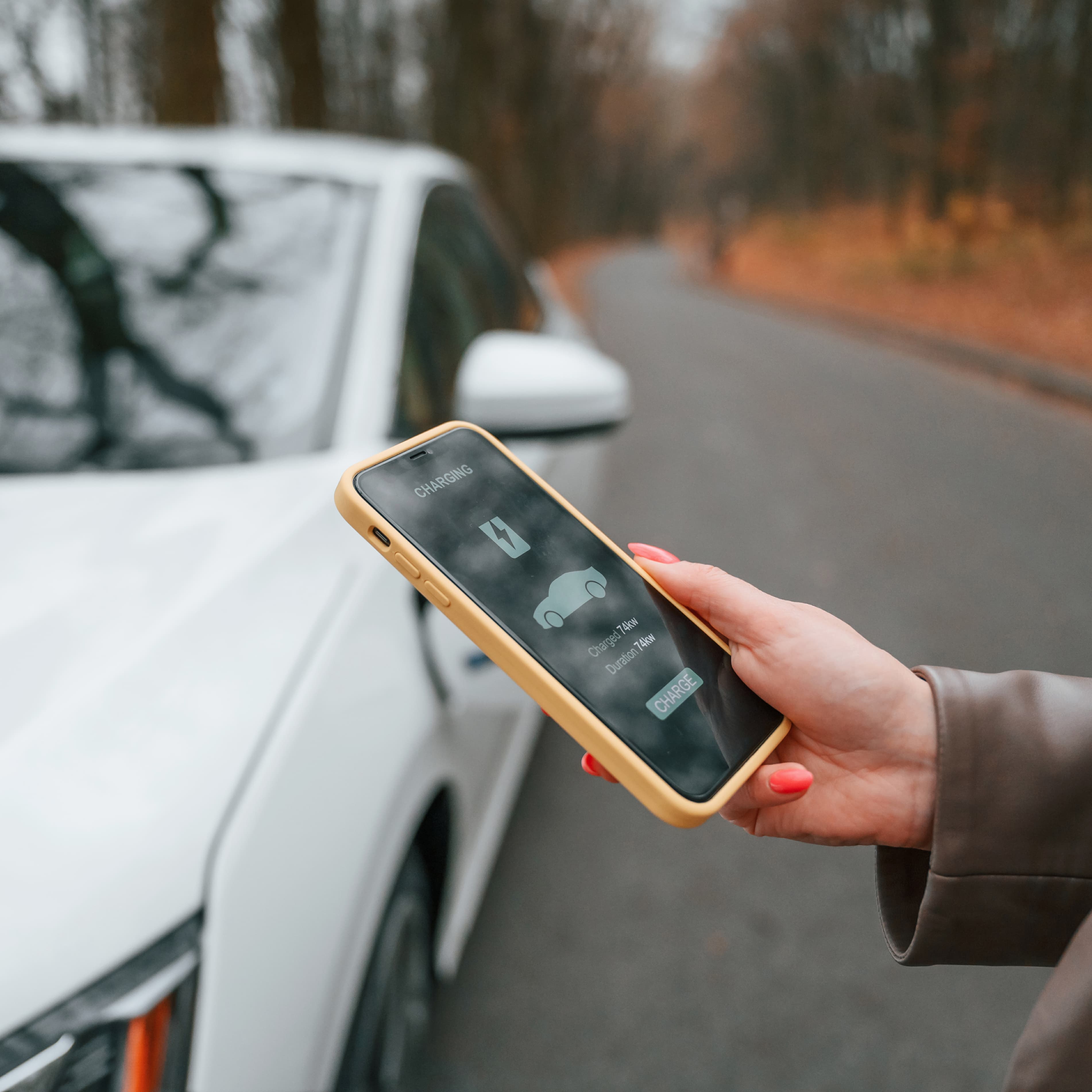 A woman holding a smartphone while standing near her car. A woman holding a smartphone while standing near her car.