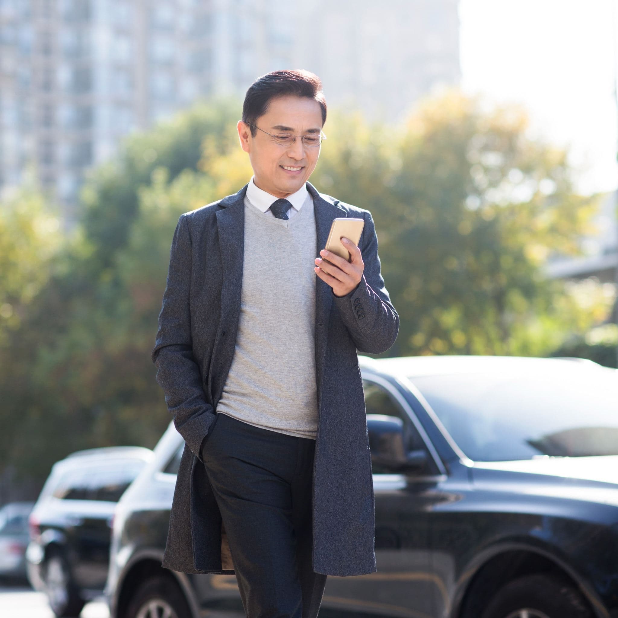 A businessman using a smartphone while standing beside a car. A businessman using a smartphone while standing beside a car.